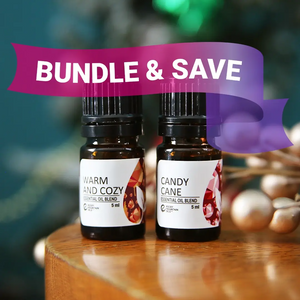 Two essential oil bottles labeled 'Warm and Cozy' and 'Candy Cane' with a 'Bundle & Save' banner on a wooden surface.